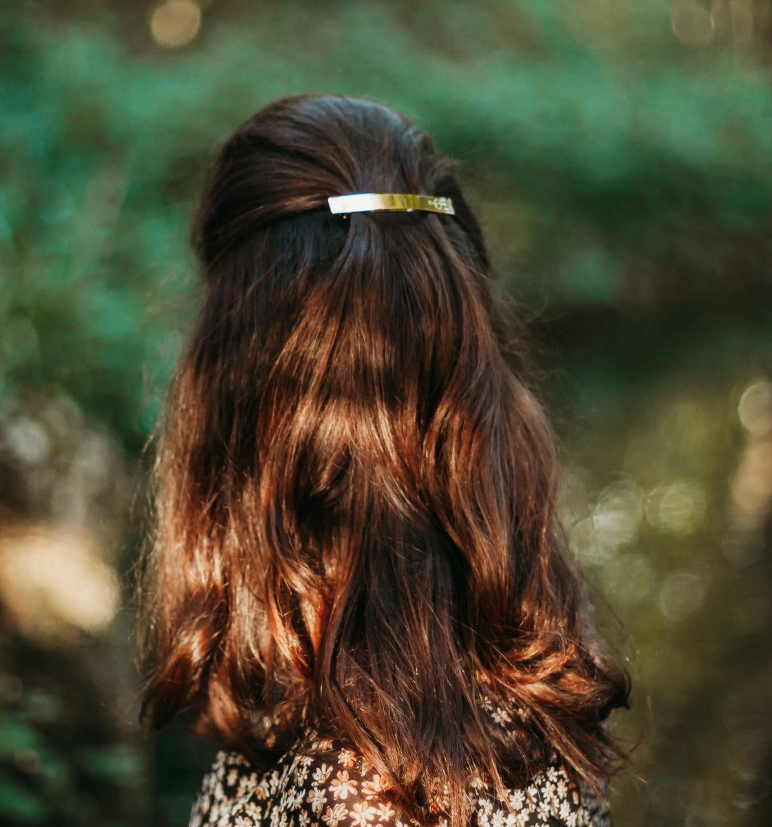 FEMME BRUNE VUE DE DOS PORTANT UNE BARRETTE DOREE LISSE SUR UNE DEMI-QUEUE