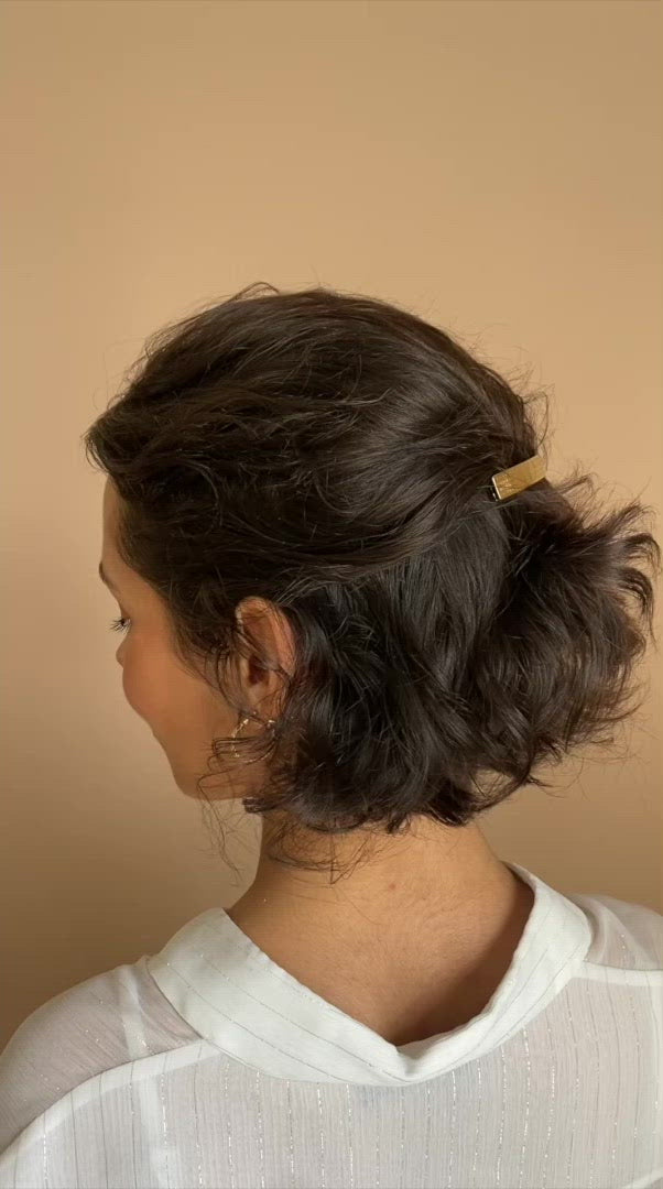 Femme aux cheveux courts mettant une barrette dorée fleurie minimaliste et élégante